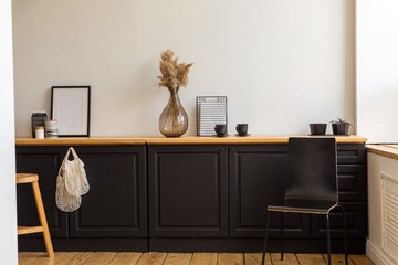 Various decorations placed on black cupboards near chair and stool in stylish room