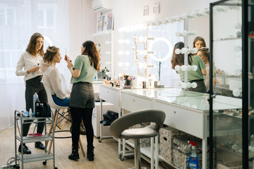 Portrait of two professional make-up artist doing makeover in lighting dressing room. Concept of backstage work.