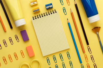 Multicolored flat layout of office or scool workplace. Notebook mockup, pencils, paper clips, tubes, eraser, pencil sharpener and other stationery on yellow background.