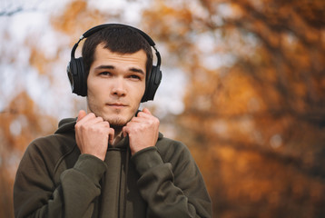 A young man walks in the Park in autumn and listens to music with headphones. Golden autumn cool weather.
