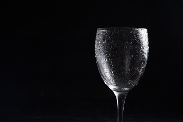 Wine glass in black and white on a black surrface with reflection and water drops