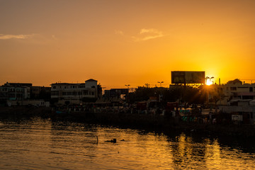 Fototapeta premium Port Sudan, Sudan. Coast silhouette in a harbor in Port Sudan, with sudanese people trading goods. Old buildings of the city in the background, beautiful orange sunset.