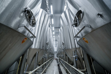 Wide angle of row of tanks in brewery. Fermentation in brewery tanks with beer for brewing. Modern beer factory. Big steel tanks for storage. Concept of brewery and beer plant.