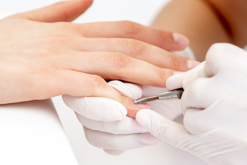 Obraz na płótnie Canvas Hands of manicurist pushing cuticles on female's nails with manicure tool. Woman receiving manicure and nail care procedure