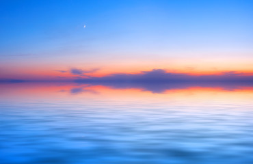 Naklejka na ściany i meble Sunset sky panorama with young moon above water surface