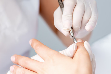 Hands of manicurist pushing cuticles on female's nails with manicure tool. Woman receiving manicure and nail care procedure