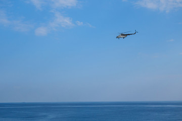 Rescue helicopter is flying above surface of sea. Blue sky is on background