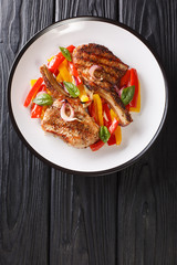 Grilled spicy pork chop with stewed yellow and red bell peppers and onions close-up in a plate on the table. vertical top view from above