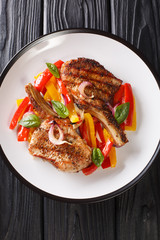 Grilled pork cutlet on the bone served with yellow and red bell peppers and onions close-up in a plate on the table. Vertical top view from above