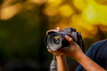 Closeup of a black camera holding by Photographer's hand with sunset background - Powered by Adobe