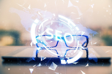 SEO hologram with glasses on the table background. Concept of search engine optimization. Double exposure.