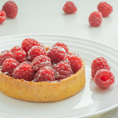 Raspberry tartlets served on a transparent plate with brown sugar. Glass of milk in the sun on a white background.