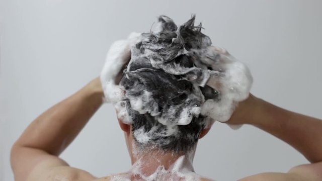 A man washes his head with shampoo on white background, rear view