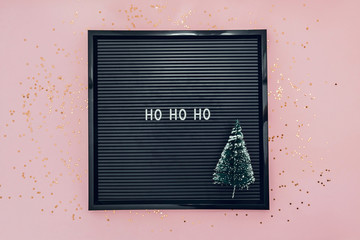 Words ho ho ho on letterboard with christmas tree on pink background with glitter confetti. New Year concept.