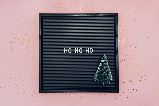 Words ho ho ho on letterboard with christmas tree on pink background with glitter confetti. New Year concept. - Powered by Adobe