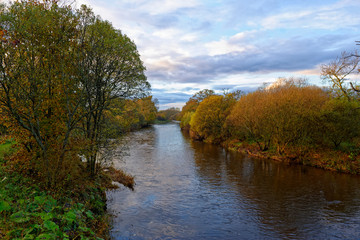 Fototapeta na wymiar The River South Esk flowing slowly through the Countryside near to the Bridge of Dun, with the trees showing their Autumn Colours.