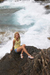 Girl sit on rocks on the sea and looking at raging waves on the Mogren in Montenegro Beach. Teenage girl sitting alone, relaxing on the nature. Tourism in Europe vacations. Journey to uncharted nature