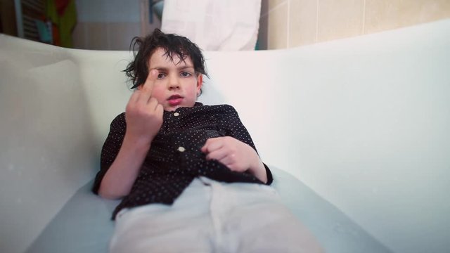 Teenager in clothes lies in water in bathroom. Shows the middle finger gesture. turbulent emotions and rebellious nature at adolescence, transitional stage of growing up and self-expression.