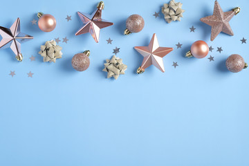 Merry Christmas concept. Flat lay Xmas composition with balls, stars, confetti, rose gold color festive decorations on blue background. Flat lay, top view, copy space.