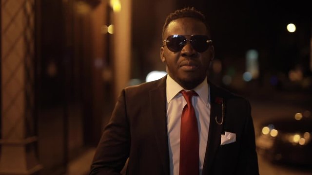 African man in black suit clothe dark sunglasses in the night city and walk