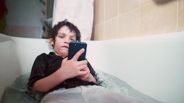 The boy uses the phone while lying in the bathroom. The transitional age is a psychologically difficult period for adolescents.