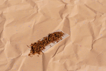 Tobacco on roll-up paper against a background of crumpled speckled paper. Selective focus
