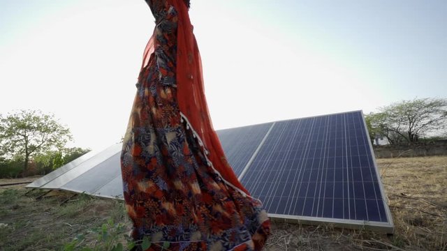 Indian woman wearing sari and carrying water jug, walks past solar panels in the Rajasthani desert. India
