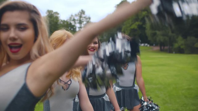 Portrait of attractive cheerleaders standing in row, raising hands with pompons and spinning around