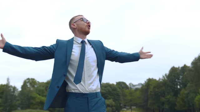 Young successful businessman standing with arms wide open in summer park