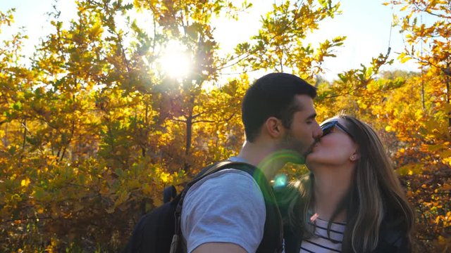 Portrait of happy smiling couple kisses while takes selfie photo with autumn garden at background. Young cheerful lovers stands at nature and looks into camera. Concept of loving. Slow motion