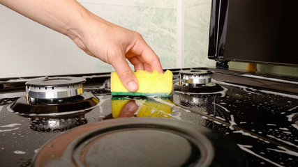 surface cleaning, woman washing gas stove with yellow washcloth and detergent