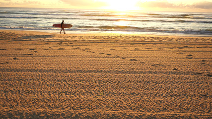 one surfer walking on the beach early morning with sunrise sunshine