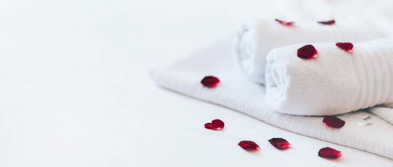 Obraz na płótnie Canvas Luxury hotel room with white spa towels on bed sheet with rose petals. Romantic holiday weekend with wellness body treatment and relax couple massage in honeymoon suite.