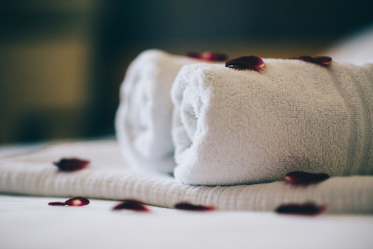 Luxury hotel room with white spa towels on bed sheet with rose petals. Romantic holiday weekend with wellness body treatment  and relax couple massage in honeymoon suite.