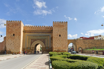 Meknes, Morocco - Okt.17,2018:Old city wall with Bab el-Khemis gate, entrance to the old city. People walking and old cars drive by. With a blue sky on a sunny day - obrazy, fototapety, plakaty