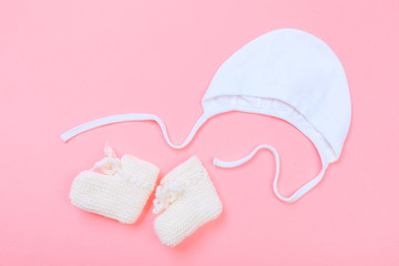 knitted baby booties and bonnet on pastel pink background .