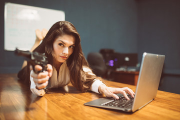 Armed sexy businesswoman aiming with pistol getting data from computer. Dangerous woman with gun...