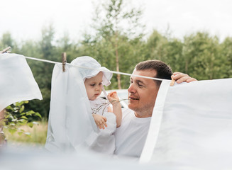 Happy father with his little daughter hangs white linen in the village in the outdoor