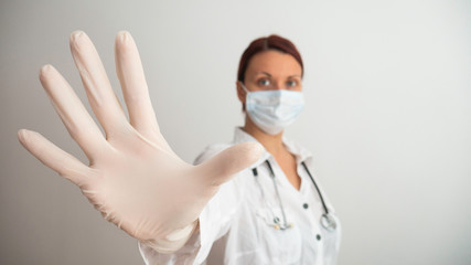 Woman with a white medical mask and latex glove shows the symbol STOP. Stopping the disease. Prevention of viruses. Negative space or copy space for text.