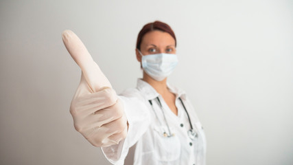 A female medical worker with a mask and gloves gives a thumbs up. The female doctor gives good news. Negative space of copy space for text.