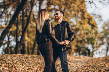 Beautiful young couple walking in the autumn park on a sunny day. They hug and smile, enjoy a walk
