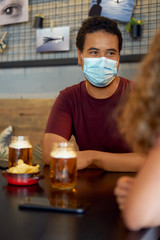 guy wearing a protective mask in a bar meeting a friend for a beer keeping the safety measures against covid disease