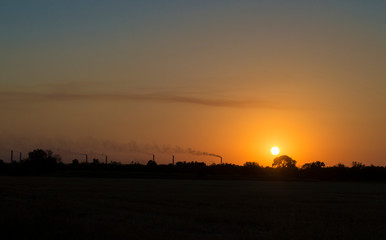 Obraz na płótnie Canvas the setting sun on the background of smoking chimneys industry