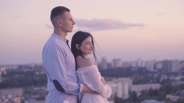 Tender couple of young lovers hugging, enjoying cityscape, romantic date on roof