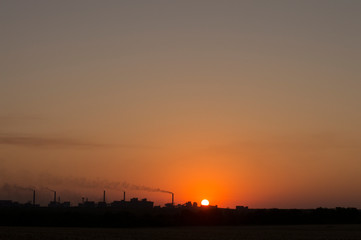 the setting sun on the background of smoking chimneys industry