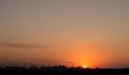 the setting sun on the background of smoking chimneys industry