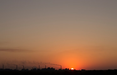 the setting sun on the background of smoking chimneys industry
