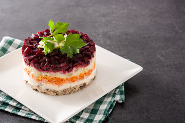 Traditional Russian herring salad with beetroot and carrots on black background. Copy space