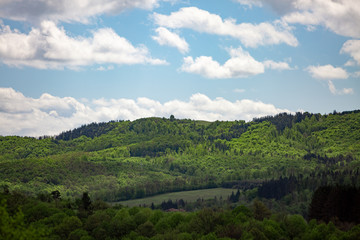 Obraz premium Scenic green rolling hills against the blue sky with clouds.