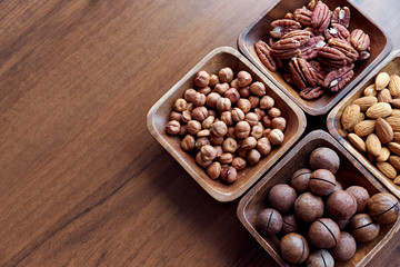 Wooden bowl with mixed nuts on table top view. Healthy food and snack. Walnut, pistachios, almonds, hazelnuts and cashews.